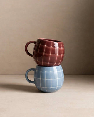Two Pool stoneware mugs stacked, burgundy over blue sky, hand-painted grid pattern