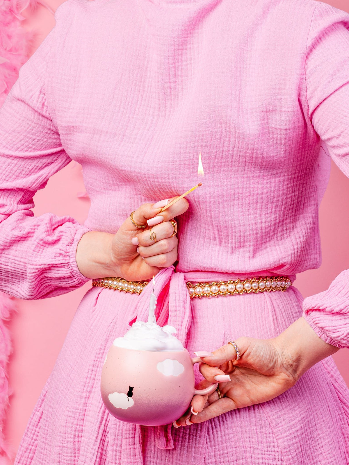 A woman dressed in pink lights the candle inside the pink Cloud mug printed with a cat on a cloud